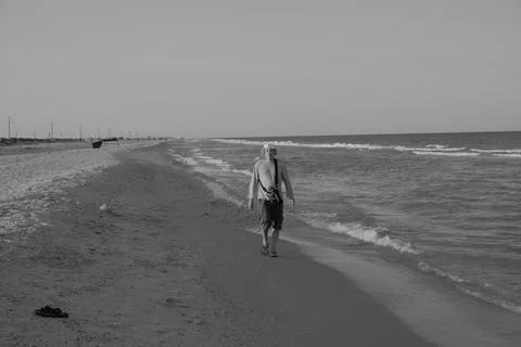 Middle-aged man walking along the seashore in summer with camera and taking Stock Photos
