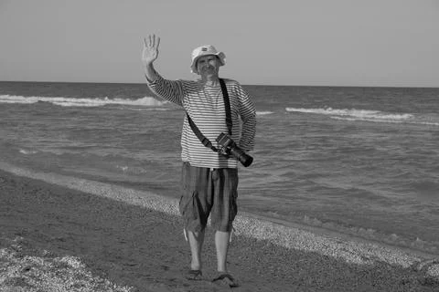 Middle-aged man walking along the seashore in summer with camera and taking Foto stock