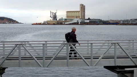 Middle-aged man walking on a bridge over water of lake or sea bay, silo and Stock Footage 231740840