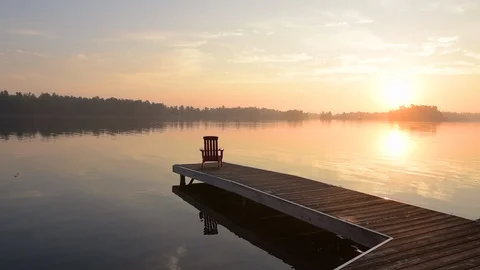 Middle aged man walking out onto dock at sunrise with coffee cup. 库存影片 94263285