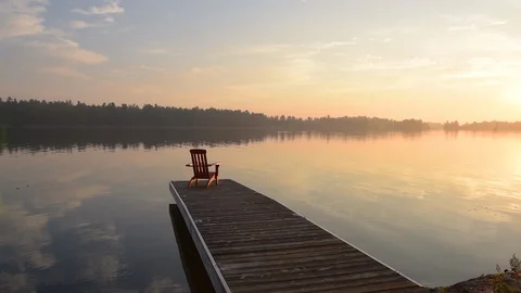 Middle aged man walking out onto dock at sunrise with coffee cup. 库存影片 95134044