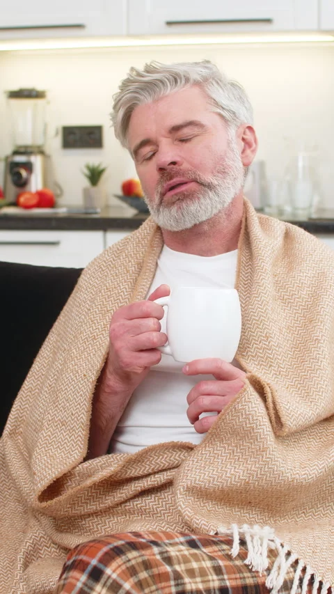 Middle-aged man warms hands on herbal tea mug enjoys aroma small sip cozy pause Stock Footage 348057527