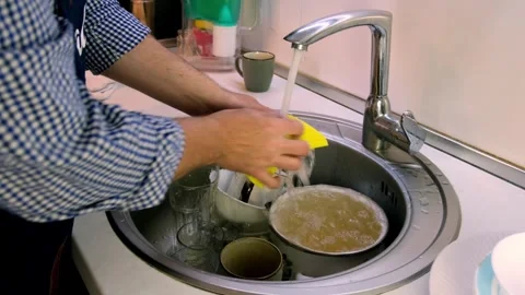A middle-aged man washes dirty dishes in his home kitchen. A man is doing h.. Stock Footage 255931093