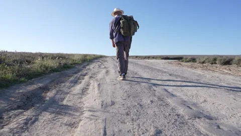 A middle-aged man wearing a hat and carrying a backpack walks alone through a Stock Footage 300424217