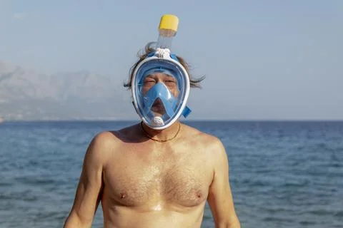 Middle aged man wearing snorkel mask stands by calm seaside 스톡 사진