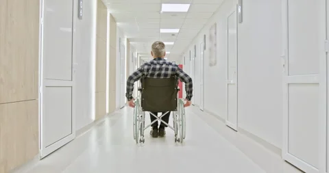 Middle-Aged Man in Wheelchair Navigating Hospital Corridor Stock Footage 276357729