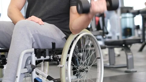 A middle-aged man in a wheelchair is working out in the gym. Lifting dumbbells Stock Footage 241521732