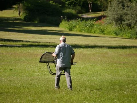 Middle aged man, when the sun is already low, carries a leisure chair Stock Photos