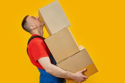 Middle-aged man in workers uniform holds large heavy boxes. Portrait of loade Stock-Fotos