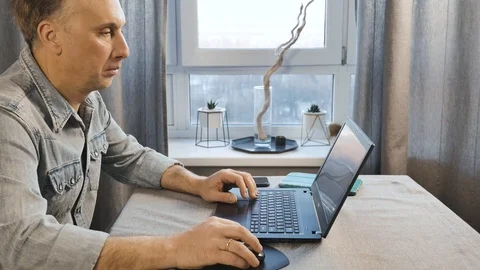 A middle aged man working on a laptop. Freelancer works at home. Side view. Video stock 99366158