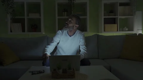 A middle-aged man working on a laptop experiences a power outage in his home. 库存影片 231004393
