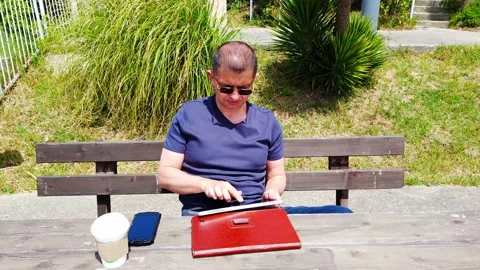 Middle-aged man works remotely in garden, in nature. Stock Footage 130874917