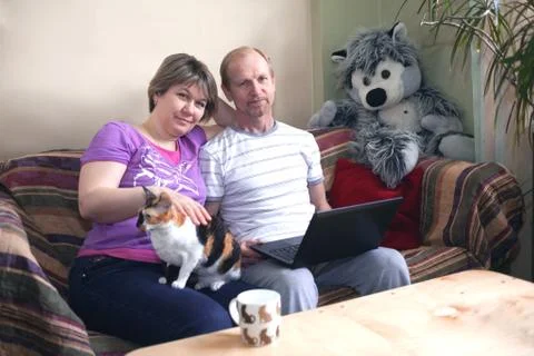 A middle-aged married couple siting at home with a laptop. On the sofa with cat Stock Photos