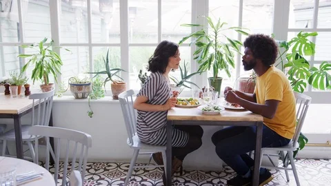 Middle aged mixed race couple eating lunch together at a table in a restaurant, 스톡 동영상 99753668