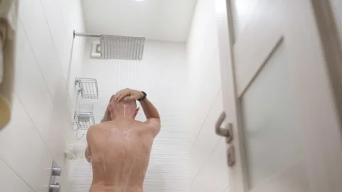 Middle-aged nacked man standing under bathroom shower and washing head with sham Stock Footage 304977856