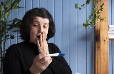 Middle aged old woman looking at pregnancy test result showing positive excited Stock Photos