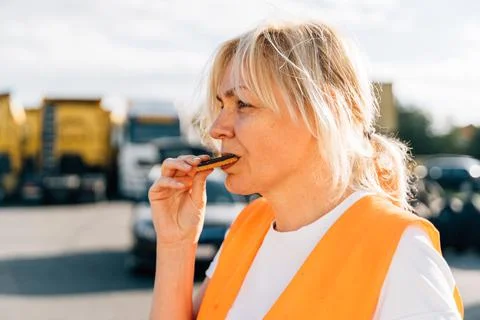 Middle aged portrait of worker engineer woman with orange vest eating cookies Stock Photos