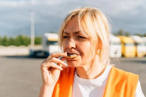 Middle aged portrait of worker engineer woman with orange vest eating cookies Stock Photos