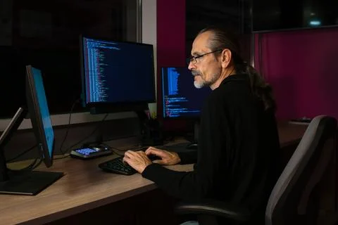 A middle-aged programmer with glasses and a ponytail works with code Stock Photos