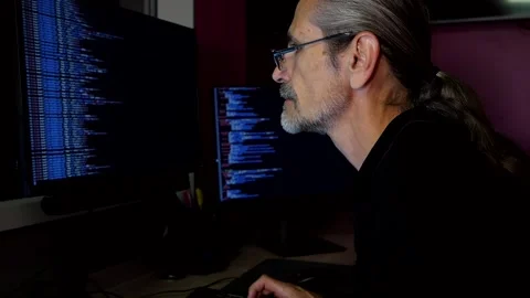 Middle aged programmer with glasses coding in a darkened office Stock Footage 247051843