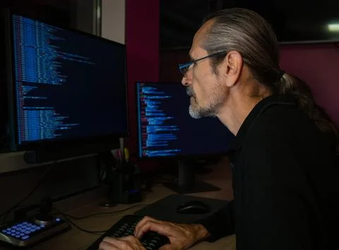 A middle-aged programmer works with code in a darkened office Stock-Fotos