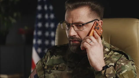 Middle-aged serviceman in eyeglasses coordinating mission via phone and laptop Stock Footage 334668784