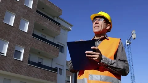 Middle-Aged Site Engineer with Hardhat Checking Clipboard at Construction Site Stock Footage 293693921