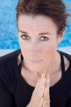 A middle aged smiling lady doing a yoga greeting, namaste, looking at camera Stock Photos