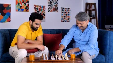 A middle-aged son and an elderly old man playing a game of chess together - q... Stock Photos
