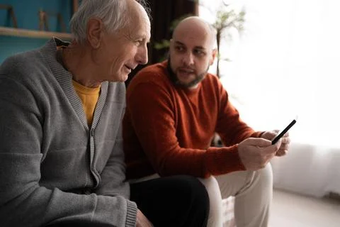 Middle-aged son helping and learning his elderly father shopping online and Stock Photos