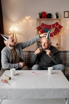 Middle-aged son helping retired father wear party hat Photos