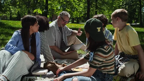 Middle Aged Teacher Explaining Lesson on Laptop to Diverse Students in Park Stock Footage 339674149