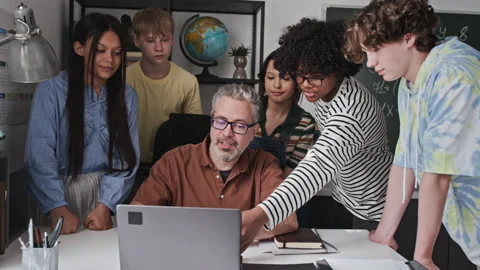 Middle Aged Teacher Explaining Lesson on Laptop to Multiethnic Teenagers 動画素材 339683091