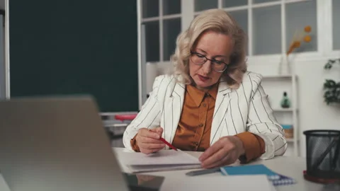 Middle aged teacher grading students papers in classroom, tutor occupation Stock Footage 251859602