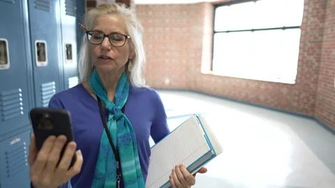 Middle-aged Teacher Smiling While Using Smartphone Video Chat in School Hallway Stock Footage 296398959