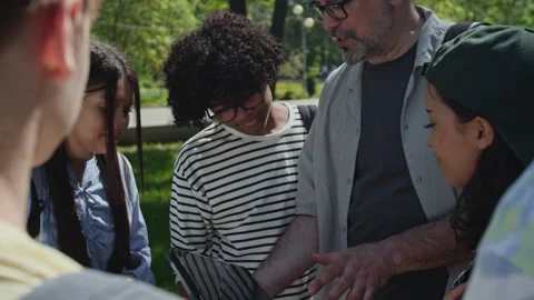 Middle Aged Teacher Using Tablet with Multiethnic Teenagers in Park Stock Footage 339675177