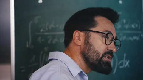 Middle-aged teacher writing equations and talking to students during math lesson Stock Footage 313493399