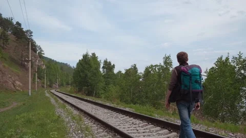 Middle aged traveler with backpack walking along rails of railway. slow motion. Stock Footage 240016615