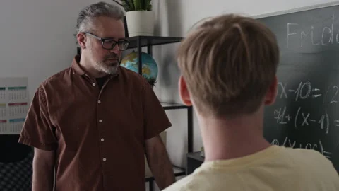 Middle-Aged Tutor Explaining Math to Teenage Boy Writing on Blackboard Stock Footage 339659421