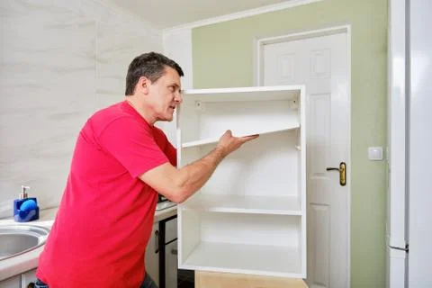 Middle aged white man installing the shelf in the kitchen cabinet. Stock Photos