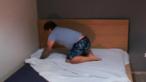 Middle aged white man tucking bedsheet close view on bed, home routine arranging Stock Footage 333578358