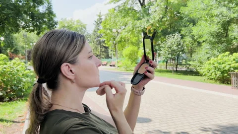 Middle-aged woman adjusts makeup on her face. She sits in park and holds in h Stock Footage 204852453
