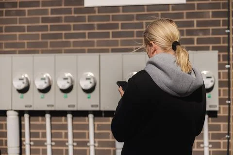 Middle-aged woman checking multiple electricity meters and recording readings Stock Photos
