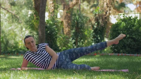 A middle-aged woman on the grass does a morning sports exercises Stock Footage 84175905