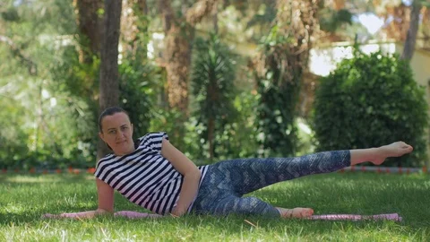A middle-aged woman on the grass does a morning sports exercises Stock Footage 84176073