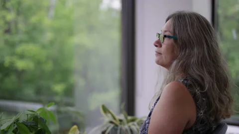 Middle aged woman looking longingly out a sunny window Stock Footage 218633123