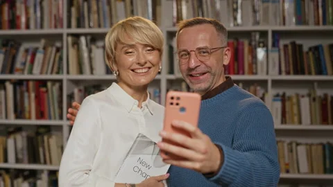 Middle Aged Woman Presenting Book to Middle Aged Man in Library Stock Footage 338046069
