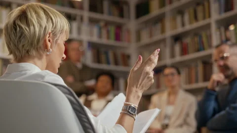 Middle-aged Woman Presenting Book to Diverse Audience in Library Stock Footage 338049149