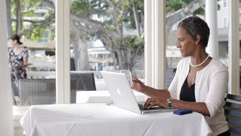 Middle-aged woman smiling while using a laptop in a restaurant. 스톡 동영상 88369027