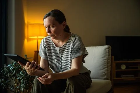 Middle-aged woman using a digital tablet while relaxing at home in the even.. Stock Photos